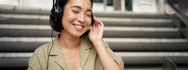 Happy Asian Girl Listens Music Headphones Smiles Sits Outdoors Stairs — Stock Photo, Image