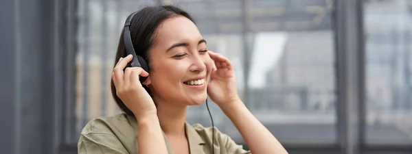 ヘッドフォンで美しいアジアの女性の肖像 市内中心部の路上で音楽を聞きます 喜んで笑顔 — ストック写真