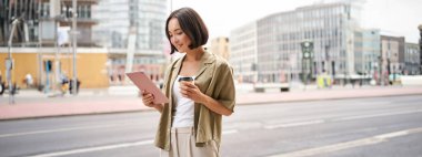 Mutlu şehir kızı sokaklarda yürüyor, tablet kullanıyor ve işe giderken kahve içiyor..