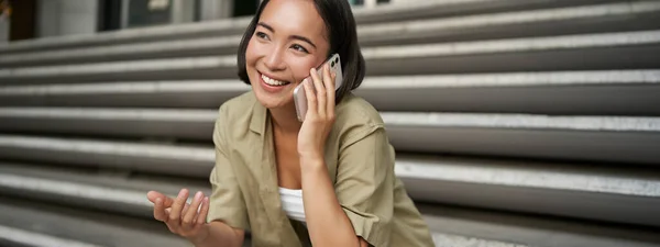 Zamknij Portret Uśmiechniętej Azjatki Rozmawia Przez Telefon Komórkowy Siedzi Zewnątrz — Zdjęcie stockowe
