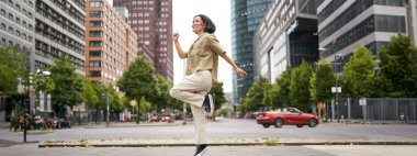 Asyalı mutlu kız portresi şehir merkezinde zıplıyor ve dans ediyor, sokaklarda poz veriyor, neşe ve heyecanı ifade ediyor. Boşluğu kopyala