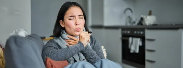 Sick korean woman coughing and feeling unwell, grimacing, has influenza, cought cold or flu, staying at home.