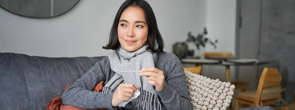 Stock image Smiling asian woman holding thermometer and looking pleased, feeling better after cold, got rid of fever, has normal temperature.