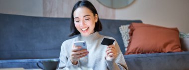 Gülümseyen Koreli kadının portresi kredi kartı ve akıllı telefon uygulaması kullanıyor, satın almak için ödeme yapıyor, internetten sipariş veriyor..