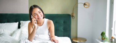 Yatakta gülümseyen Koreli kız, cep telefonuyla konuşan, telefon görüşmesi yapan, Asyalı kadının akıllı telefondan sipariş verdiği tembel bir sabah..