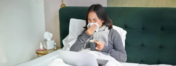 Woman with cold, having flu, staying in bed, sneezing in napkin, runny nose and influenza symptoms. Copy space