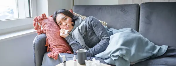 Sick woman lying on sofa at home, catching cold. Young girl freezing from heating problem in her apartment, concept of high cost of living.