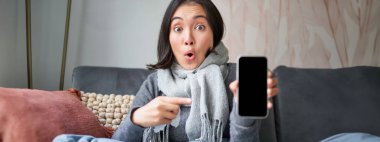 Gülümseyen kızın evde hasta kalmasının, cep telefonu ekranını göstermesinin, online tıbbi başvuru, eczane veya akıllı telefondan GPS tavsiye etmesinin portresi.