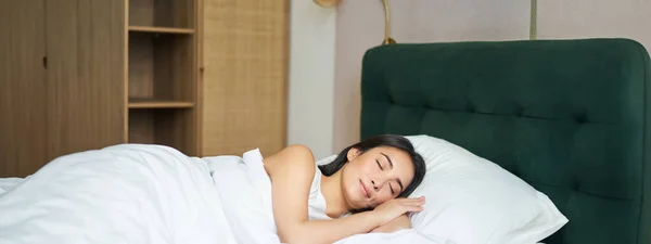 Beautiful asian girl sleeping in her bed, lying in bedroom with closed eyes under white sheets, warm winter duvet.