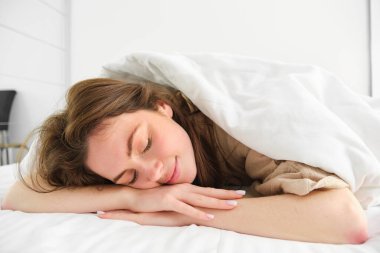 Güzel bir genç kadın battaniyenin altında uzanıyor ve gülümsüyor, uyuyor, güzel bir sabah uykusu çekiyor, yatakta tembel bir gün geçiriyor. Yaşam tarzı ve ev kavramı