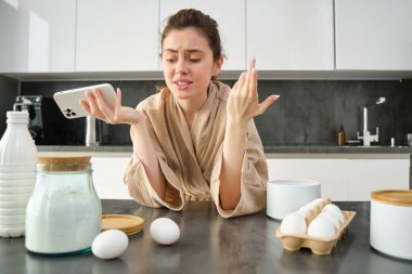 Çekici, genç, neşeli kız mutfakta yemek pişiriyor, para kazanıyor, yemek tarifi kitabını tutuyor, fikirleri var..