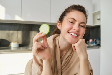 Yemek ve yaşam tarzı konsepti. Güzel bir kadın mutfakta yemek pişiriyor, elinde çiğ kabakla gülümsüyor, sağlıklı vejetaryen yemeği hazırlıyor, salata yapıyor, mutlu görünüyor..