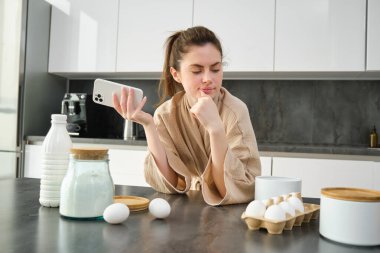 Çekici, genç, neşeli kız mutfakta yemek pişiriyor, para kazanıyor, yemek tarifi kitabını tutuyor, fikirleri var..