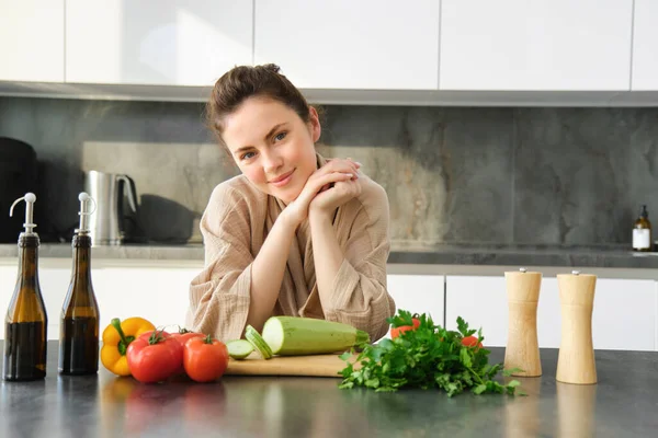 Portrait of beautiful young woman in her home clothes, chopping vegetables, holding knife and cutting zucchini, cooking in kitchen, preparing food for family dinner.