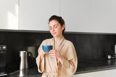 Mutlu genç bir kadının portresi güne bir fincan kahveyle başlar, fincandan çay içer, mutfakta durur, neşeyle gülümser..