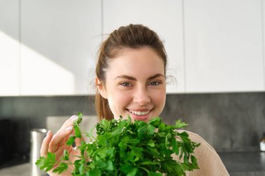 Bir buket maydanozla gülümseyen güzel bir kızın portresi, mutfakta durup yemek pişirmek, sağlıklı taze salata ya da yemeğe şifalı otlar eklemek,.