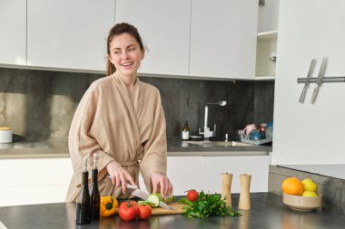 Güvertede sebze doğrayan mutlu bir kadının portresi, mutfakta dikilmek, kendi kendine yemek pişirmek, sağlıklı yemekler, lezzetli taze salata hazırlamak ve gülümsemek..