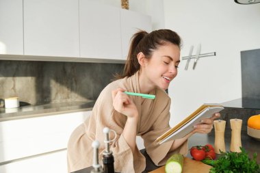 Mutfakta yemek pişiren, notlarını okuyan, yemek hazırlarken yemek tarifini kontrol eden, salata hazırlayan, alışveriş listesini yazan kadın portresi..