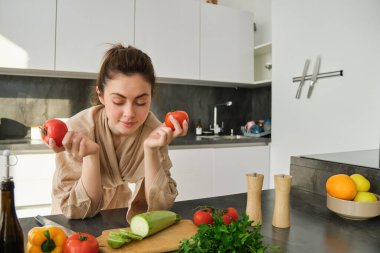 Mutfakta evde yemek yapan, elinde domates tutan, sebzeli taze yemek hazırlayan, doğrama tahtasının yanında duran bir kadının portresi..