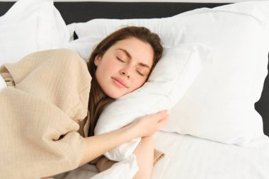 Mutlu, güzel genç bir kadının portresi. Yatakta dinleniyor, pijama giyiyor, yastığına sarılıyor ve uyurken gülümsüyor..