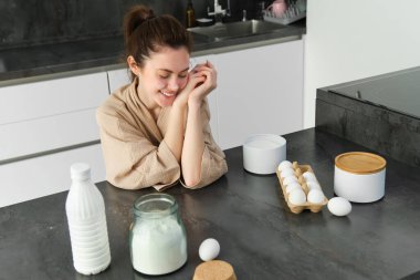 Çekici, genç, neşeli kız mutfakta yemek pişiriyor, para kazanıyor, yemek tarifi kitabını tutuyor, fikirleri var..