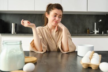 Çekici, genç, neşeli kız mutfakta yemek pişiriyor, para kazanıyor, yemek tarifi kitabını tutuyor, fikirleri var..