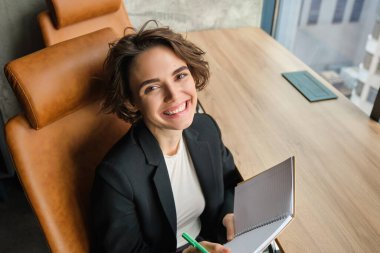 Ofiste çalışan kendine güvenen bir satış elemanının portresi, iş odasında oturuyor, okuyor, sunum için düşüncelerini yazıyor, notlar alıyor, pencerenin yanında oturuyor, toplantı için hazırlanıyor..