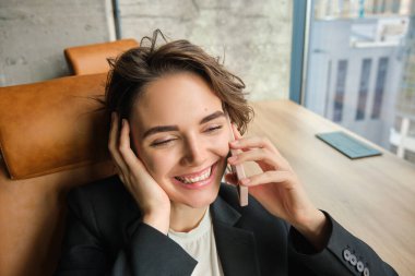 Güzel ofis müdürünün yakın portresi, ofisinde oturan çalışan, bir telefon görüşmesi sırasında gülen ve gülümseyen, akıllı telefon tutan, öğle yemeği molasında dinlenen.