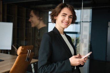 Şirkette çalışan satış elemanı portresi, cam duvarın yanında duran, cep telefonu tutan, gülümseyen, müşteriyi arayan, iş görüşmesi ayarlayan..