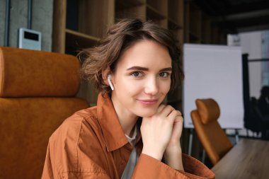 Gülümseyen genç bir kadının yakın portresi, ofis çalışanı konferans odasında oturuyor, kameraya mutlu bakıyor..