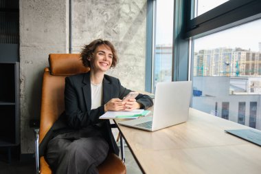 Ofisinde çalışan bir kadının portresi. Başarılı iş kadını dizüstü bilgisayarı ve telefonuyla oturuyor, gülümsüyor ve mutlu görünüyor..