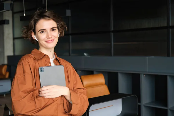 Portrait of young woman, company employee, office worker in casual clothes working with tablet in conference room, planning team meeting.