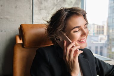 Şirket insanları ve iş kavramı. Takım elbiseli genç bir kadın, ofiste oturuyor ve sohbet ediyor, telefona cevap veriyor ve gülümsüyor, müşteriyle konuşuyor..