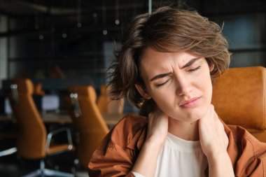 Kadın çalışanın portresini kapat, yönetici boynuna dokunur ve bütün gün çalıştıktan sonra ağrı hisseder, kaslara masaj yapar..