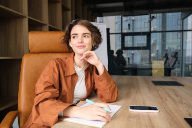 Genç bayan girişimcinin portresi, ofiste çalışan, yazan, konferans odasında notlar alan, gülümseyen.