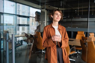 Genç dijital göçebe portresi, ofiste çalışan kadın, konferans odasında akıllı telefonuyla dikilen, günlük kıyafetler giyen..