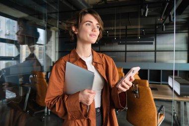 Ofiste çalışan, dijital göçebe portresi. Akıllı telefon kullanıyor, dizüstü bilgisayar tutuyor..