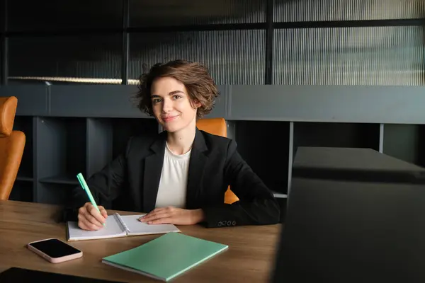Portrait of successful brunette woman in suit, corporate manager in office, writing, preparing documents for meeting, reading case.