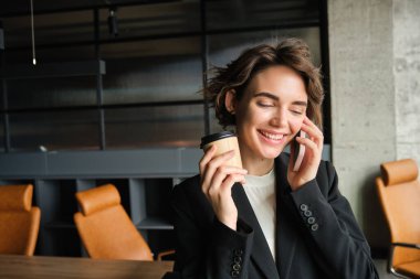 İş kadını portresi cep telefonuyla konuşur, ofiste durur ve kahve içer..
