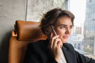 Ofiste çalışan güzel bir kadının portresini yakın çekim, telefona cevap vermek, telefonla konuşmak ve gülümsemek..