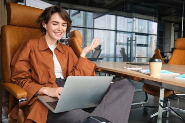 Online toplantı sırasında iş projesini tartışan bir kadının portresi, dizüstü bilgisayara bakmak, ofiste çalışmak, iş arkadaşıyla konuşurken el kol hareketi yapmak..