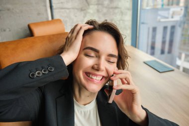 Cep telefonuyla konuşan kurumsal bir kadının portresi, ofisindeki bir telefona cevap vermek, gülmek, gülümsemek, sohbet etmek, sandalyesine yaslanmak..