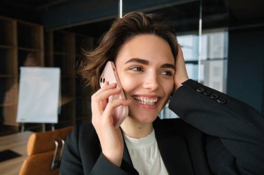 Ofisinde mutlu bir kadının portresini yakından çek. İş kadını telefonuna neşeli bir gülümsemeyle cevap veriyor. Telefonda harika haberler alıyor..
