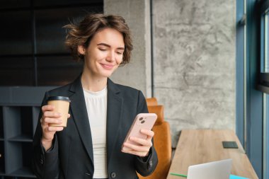 Genç müdürün portresi, ofiste çalışan takım elbiseli bir kadın, elinde kahve ve akıllı telefon, cep telefonunda gülümseyen yüzüyle mesajlar okuyor..