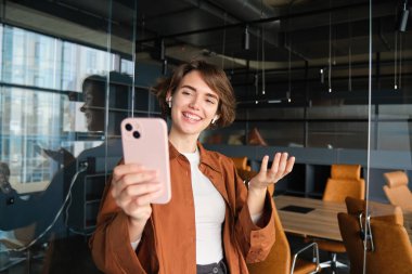 Genç sosyal medya yaratıcısının portresi, şirket için içerik oluşturan kadın, akıllı telefondan video kaydı, cep telefonuyla online toplantıya katılıyor, günlük kıyafetlerle poz veriyor..