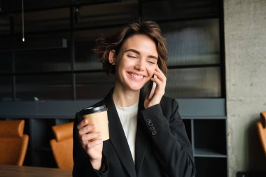 İş kadınının akıllı telefondan müşteriyi araması, telefona cevap vermesi konferans odasında durup kahve içmesi. Ofiste çalışan genç bayan girişimci..