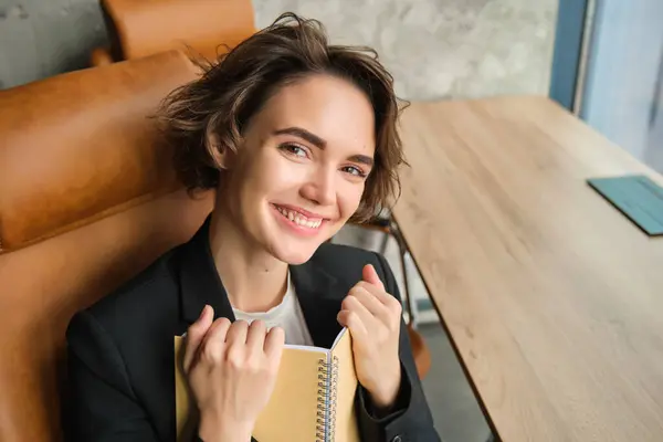 Portrait of happy businesswoman with notebook, holding her diary or planner, sitting in office and smiling.