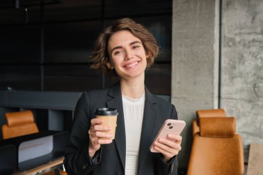 Başarılı kadın girişimci imajı, iş kadını ofisinde kahve içiyor ve cep telefonu tutuyor.