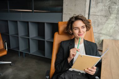 Güzel, çalışkan bir satıcının resmi, ofisinde çalışıyor, evrakları yazıyor, sözleşmeleri okuyor, pencerenin önünde oturuyor ve gülümsüyor..