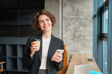 Ofiste çalışan bir kadının portresi, müdür kahve içiyor ve elinde cep telefonu kullanıyor..